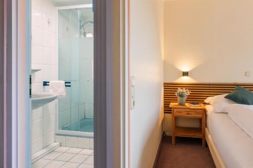 a bathroom with a shower and a bed and a sink at Hotel Thesdorfer Hof in Pinneberg