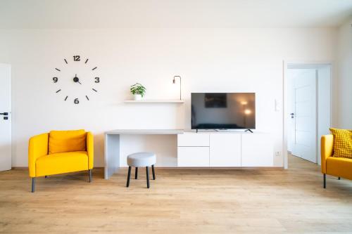 a living room with two yellow chairs and a table and a clock at Pálava Lake Apartments in Pasohlávky