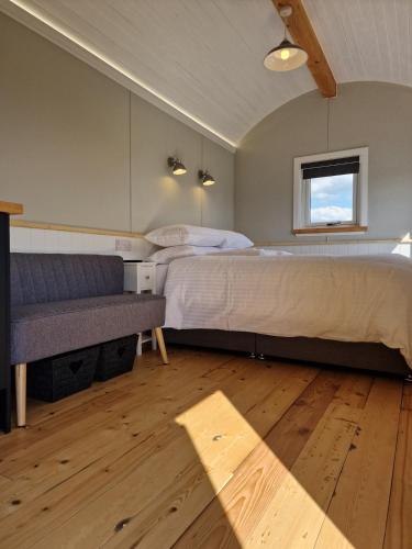 a bedroom with a bed and a couch and a window at Long Meadow Shepherd Hut - Brecon Beacons, LD3 7TD in Tal-y-llyn