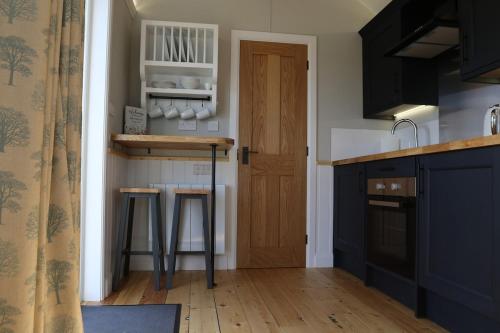 a kitchen with black cabinets and a counter with stools at Long Meadow Shepherd Hut - Brecon Beacons, LD3 7TD in Tal-y-llyn