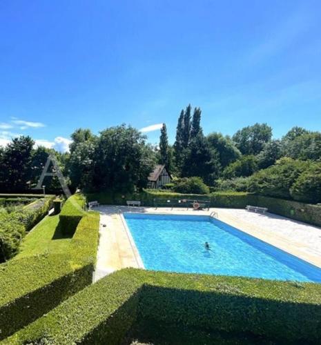 une grande piscine entourée de haies vertes dans l'établissement Appartement cosy avec piscine chauffée, à Cabourg