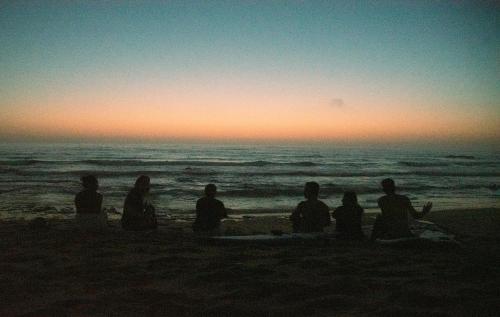 a group of people sitting on the beach watching the sunset at 70's Hostel in Ericeira