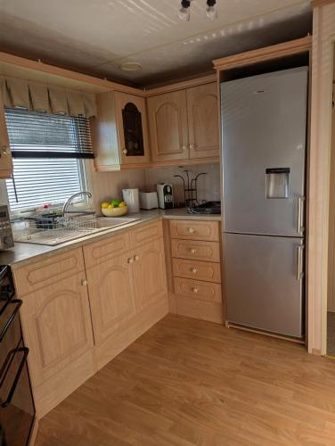 a kitchen with wooden cabinets and a stainless steel refrigerator at Aberystwyth holiday village walking distance to beach, town great outside space parking next to property in Aberystwyth