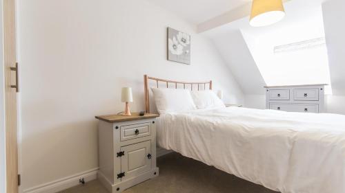 a bedroom with a white bed and a nightstand with a lamp at The Crows Nest Apartment in Plymouth