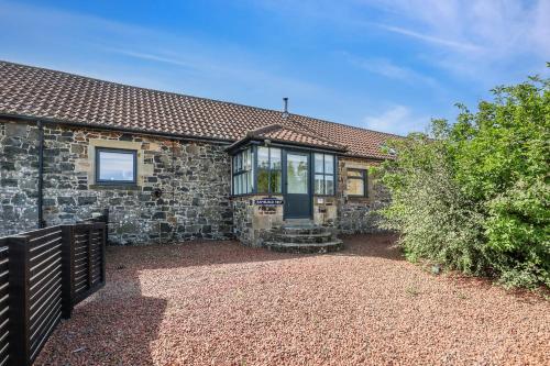 a stone house with a black door and a fence at Stable Cottage - North East Escapes in Bamburgh