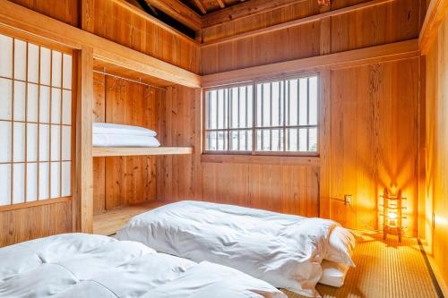 two beds in a room with wooden walls and windows at わらほんど in Naha
