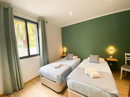 2 camas en una habitación con paredes verdes y ventana en Casa Trevo de 4 Folhas, en Furnas
