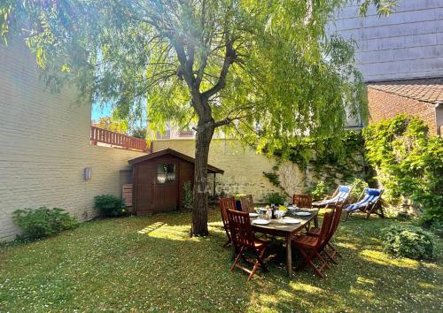 une table et des chaises dans une cour avec un arbre dans l'établissement Maison de famille L'Amandoise, à Le Touquet-Paris-Plage