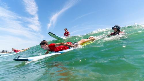 a group of people riding a wave on surfboards in the ocean at Watermen's Cabana 2B - 2-Bed, 1-Bath - Walk To BEACH Access & PET Friendly! in Waves