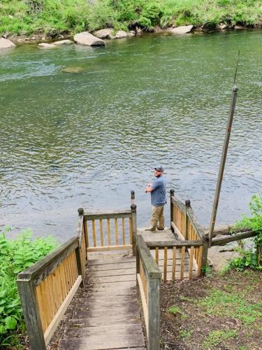 a man standing on a wooden bridge over a body of water at River's Edge in Cullowhee