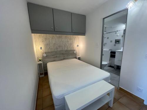 Cette petite chambre comprend un lit blanc et un miroir. dans l'établissement T1 bis rénové et cosy à côté des Thermes et de l'étang de Thau, à Balaruc-les-Bains