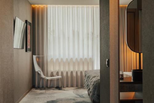 a bedroom with a bed and a chair next to a window at Hotel Leiriartem by Grupo Quinta dos Lagos in Leiria
