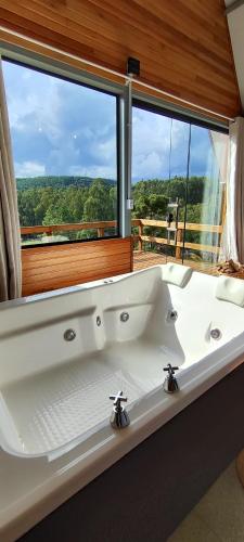 a white bath tub in front of a large window at Cabana Santa Cruz 2 in São Francisco de Paula