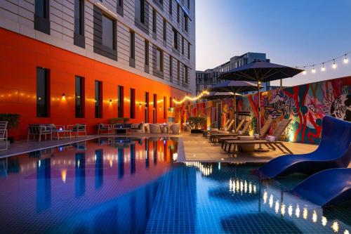 a pool with chairs and umbrellas next to a building at Aloft Dubai South in Dubai