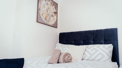 a bed with a blue headboard and two towels at Modern, comfy 2 bedroom House in Hatfield, town centre, free parking, large garden in Hatfield