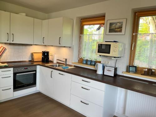 eine Küche mit weißen Schränken und einer Spüle und einer Mikrowelle in der Unterkunft Ferienhäuser am Vogelpark - Boddenhaus 60 in Marlow