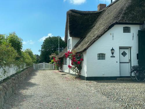 a white cottage with a thatched roof and flowers on the side at Haus Wattwurm in Midlum