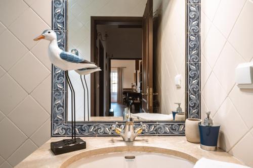 a mirror with a bird statue on a bathroom sink at Casa da Hera in Ericeira