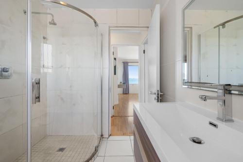 a white bathroom with a shower and a sink at Sea Spray B306 in Bloubergstrand