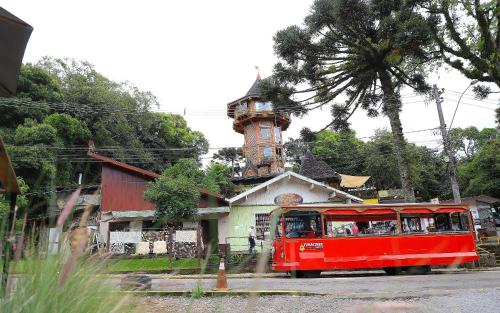 a red trolley driving past a building with a tower at Pousada Vista do Lago: Lazer e família em Gramado! in Gramado