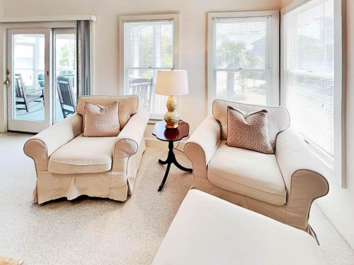 two white chairs in a living room with windows at Mercy Me in Tybee Island