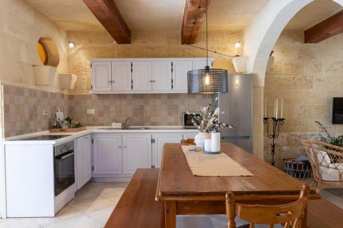 a kitchen with white cabinets and a wooden table at Gozobreak Farmhouses in Kerċem