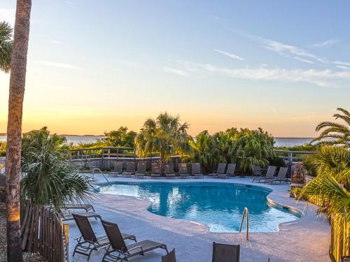 a resort pool with chairs and the ocean in the background at Bay View Villas 106 in Tybee Island