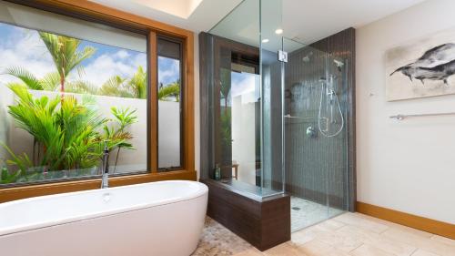 ワイコロアにあるELEGANT ESCAPE Elegant 4BR Laulea Home with Pool and Ocean Viewの浴槽とガラスのシャワー付きのバスルーム