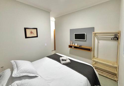 a bedroom with a white bed and a television at Casa Lago da Dinda 3 in Espirito Santo Do Pinhal