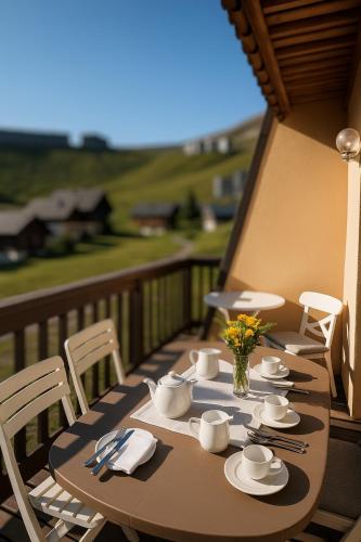 une table en bois avec des tasses et des soucoupes sur un balcon dans l'établissement Les Chalets de Mel, à Saint-Lary-Soulan