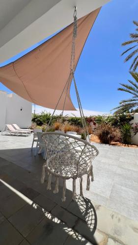 a swinging chair with an umbrella on a patio at Villa Le Domaine Djerba Piscine Chauffée sans vis à vis in Mezraya