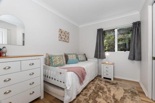 a white bedroom with a bed and a window at Nana Glads of Paihia in Paihia