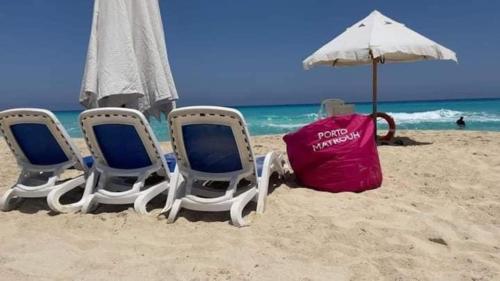 three chairs and an umbrella on a beach at Porto Matrouh Majestic in Marsa Matruh