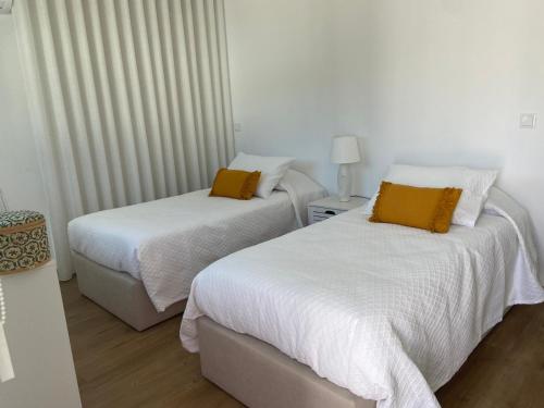 two beds in a room with white sheets and yellow pillows at Casas Peralta - Outeiro in Arouca