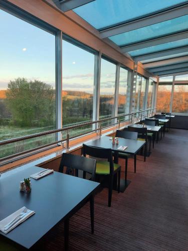 a restaurant with tables and chairs and large windows at L'Hôtel et Restaurant du Golf de Clervaux in Eselborn