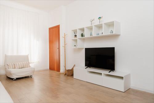 een witte woonkamer met een televisie en een stoel bij La Maison Calasetta in Calasetta