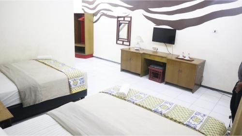 a bedroom with a bed and a desk and a television at PLUM Hotel Palereman Batu in Batu