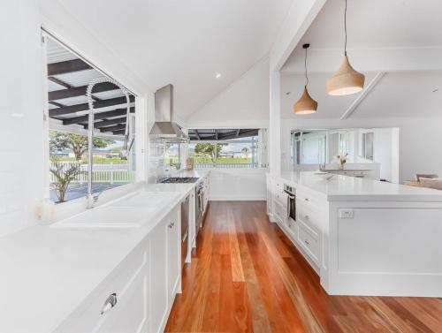 a kitchen with white cabinets and wood floors at Hamptons White House in Murwillumbah