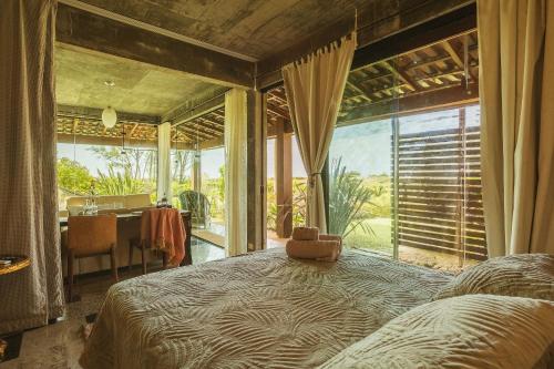 a bedroom with a bed in front of a large window at Villa Bali Casas pé na areia in Barra de Ibiraquera