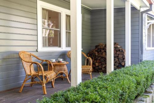 a porch with two chairs and a table and a pile of logs at Brae View House - By Latitude South Coast in Berry