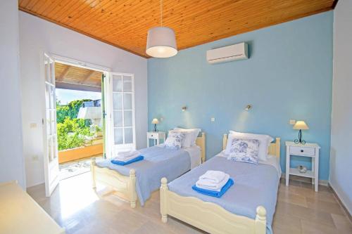 two beds in a blue room with a window at Villa Maistro Cottage by Villa Plus in Ágios Stéfanos