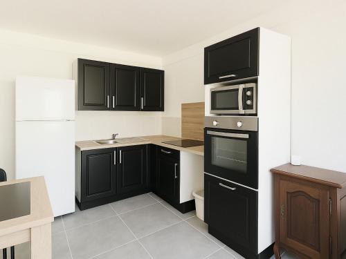une cuisine avec des armoires noires et un four micro-ondes dans l'établissement Appartement neuf à 50m de la plage centrale, moderne et tout confort - FR-1-732-61, à Argelès-sur-Mer