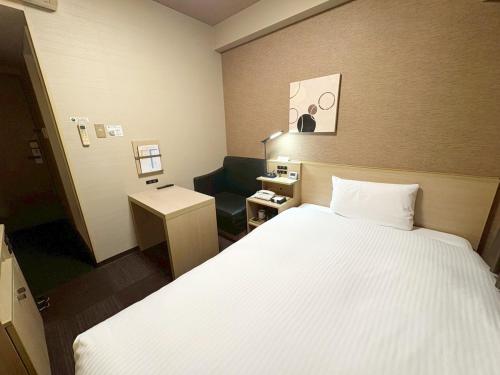 a hotel room with a bed and a chair in it at Hotel Route-Inn Higashihiroshima Saijo Ekimae in Higashihiroshima