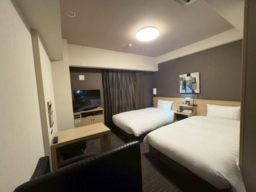 a hotel room with two beds and a television at Hotel Route-Inn Higashihiroshima Saijo Ekimae in Higashihiroshima