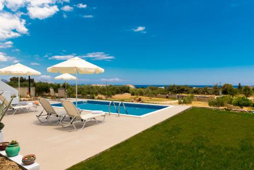 a swimming pool with chairs and umbrellas next to a yard at Orianna Sea View Villa in Gennadi