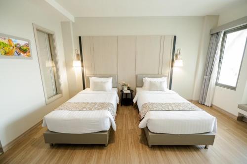 two beds in a room with white walls and wood floors at THE NAVY HOUSE HOTEL in Sattahip