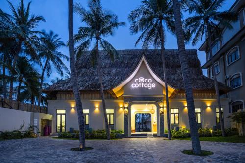 a hotel with palm trees in front of a building at Coco Cottage Beachfront Resort in Mui Ne