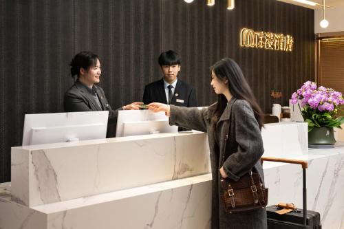 a woman standing in front of a counter with two men at Baiman Hotel Beijing South Railway Station Heyi Subway Station Branch in Beijing
