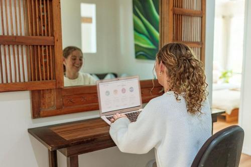 a woman sitting at a table with a laptop in front of a mirror at Ocean views Close to Coolum Pet friendly Firepit Mountain Views in Yandina Creek