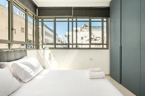 a bedroom with a large white bed and windows at Eclectic Blue Apartment on Sheinkin by Sea N' Rent in Tel Aviv